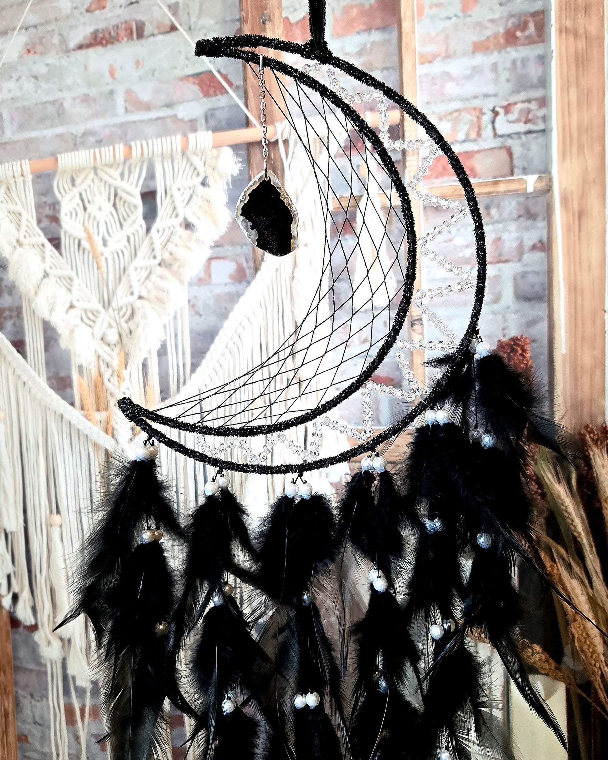 close up of crescent moon dream catcher with black feathers and hanging geode