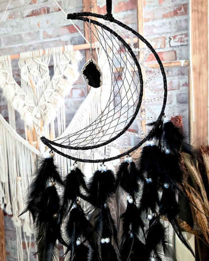 close up of crescent moon dream catcher with black feathers and hanging geode