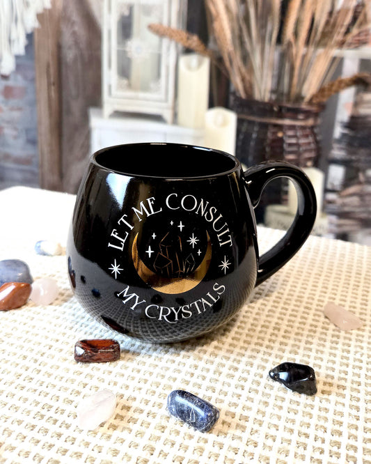 black coffee mug that says let me consult my crystals with moon and crystal design in gold